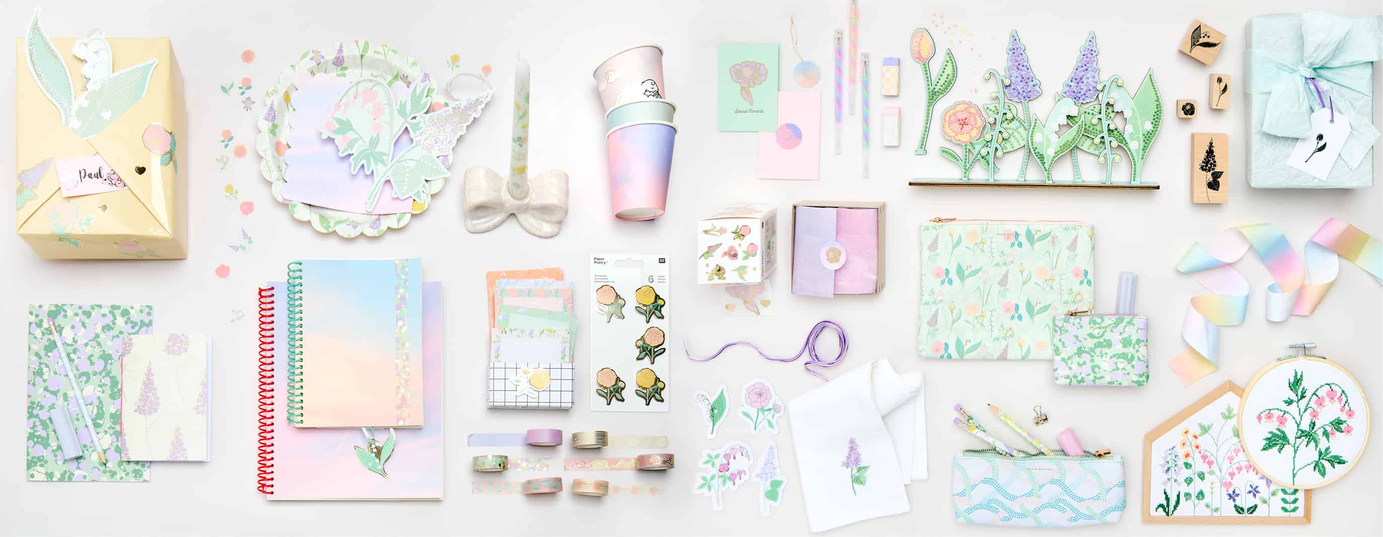 Papeterie-, Partyartikel, Stickbilder und Dekorationen mit Himmel- und Blumendesigns liegen angeordnet auf grauem Hintergrund. 