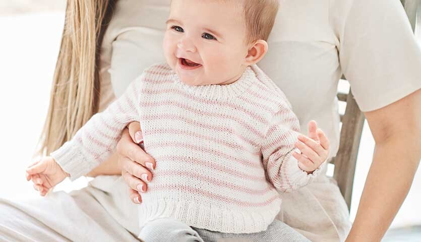 Strickanleitung Pullover aus Baby Organic Cotton: Baby in gestreiftem Pullover auf dem Schoß einer Frau.
