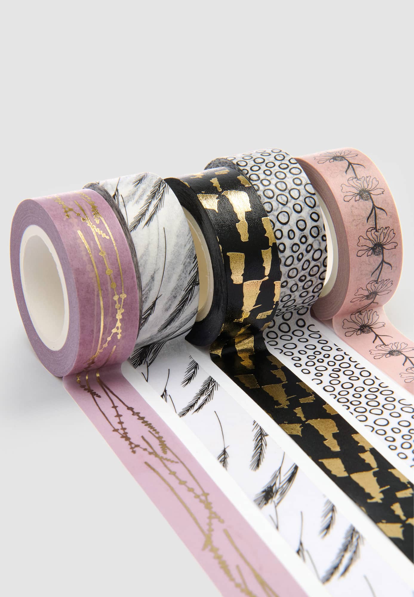 Ausgerollte Washi Tape mit abstrakten Mustern liegen aneinandergereiht auf grauem Hintergrund.