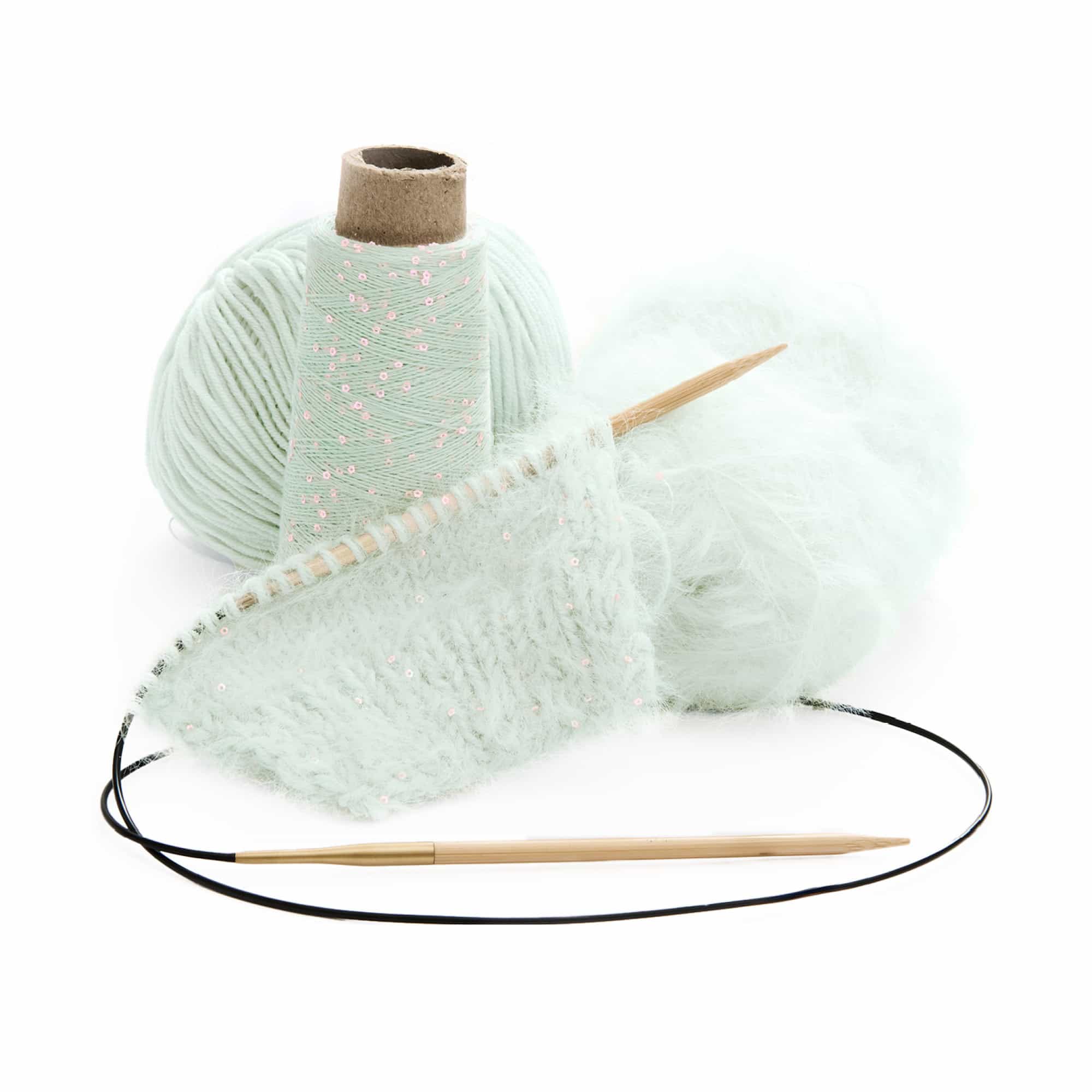 Angestricktes Strickstück an Stricknadeln vor Wollknäuel