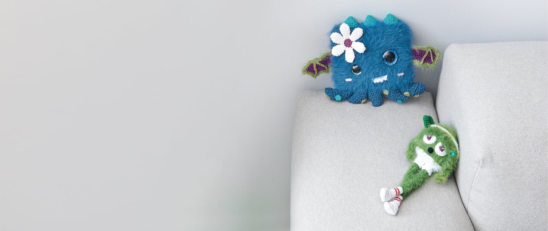 Zwei gehäkelte Monster sitzen auf einer Sofalehne.