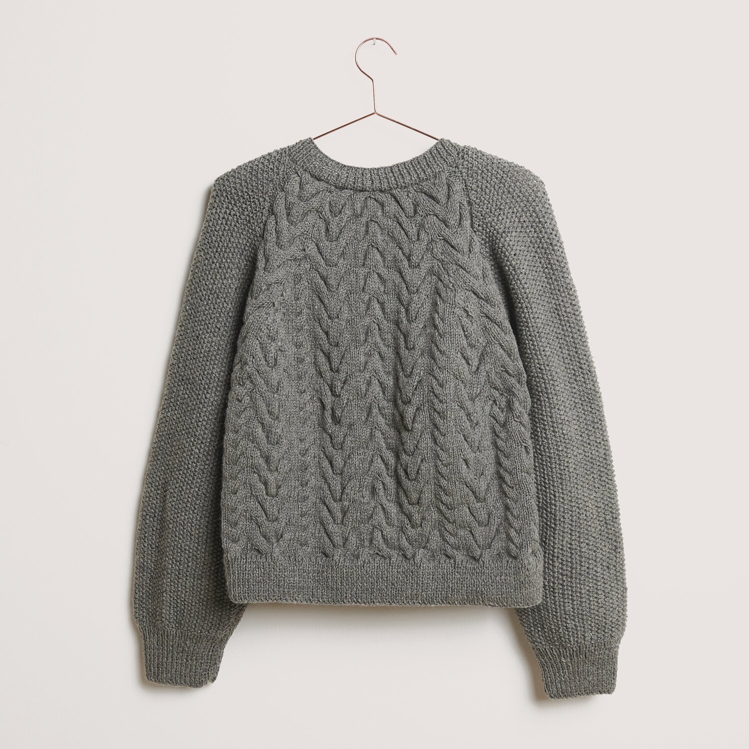 Essentials Soft Merino aran Pullover in Mittelgrau, gestrickt aus Rico Design Wolle, hängt an einem Kleiderbügel vor neutralem Hintergrund.