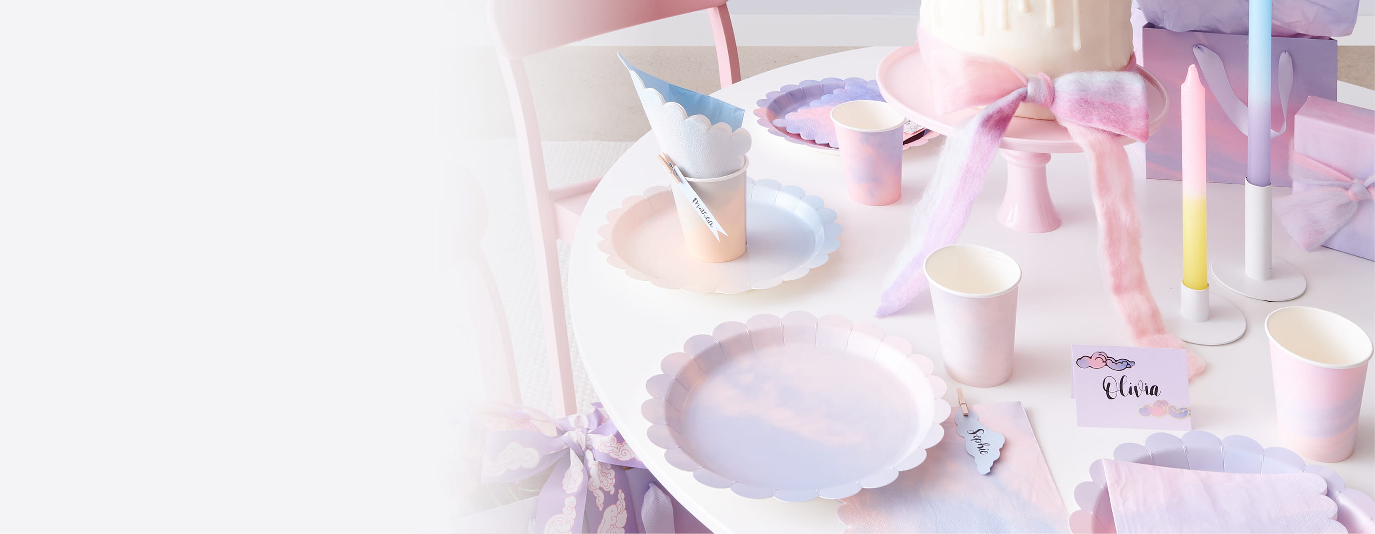 Ein Tisch ist in Pastelltönen mit Pappteller, -becher, Servietten und Dekoration gedeckt.