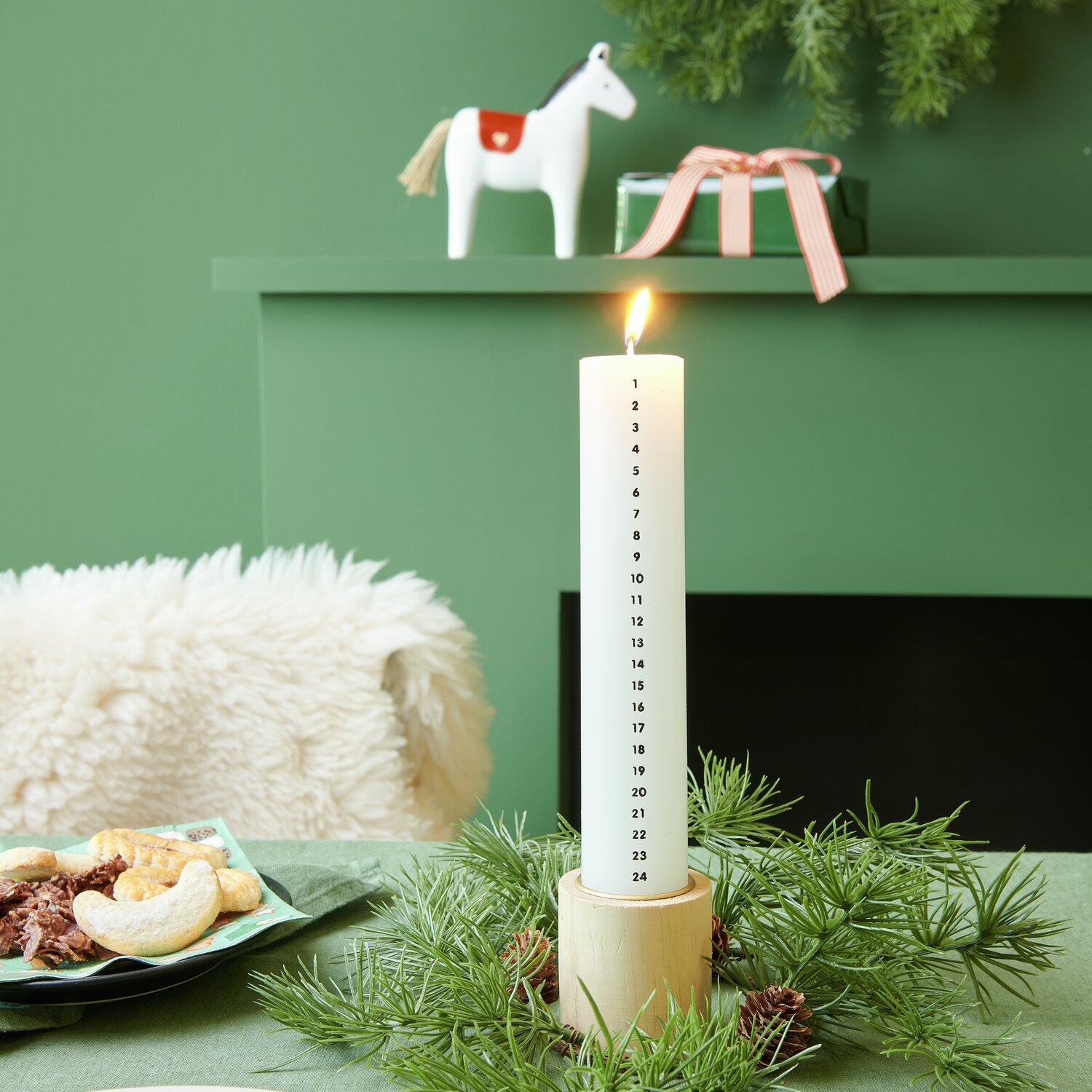 Adventskalender Kerze, Ø4x20cm, in einem weihnachtlichen Arrangement mit Tannenzweigen und Keksen.