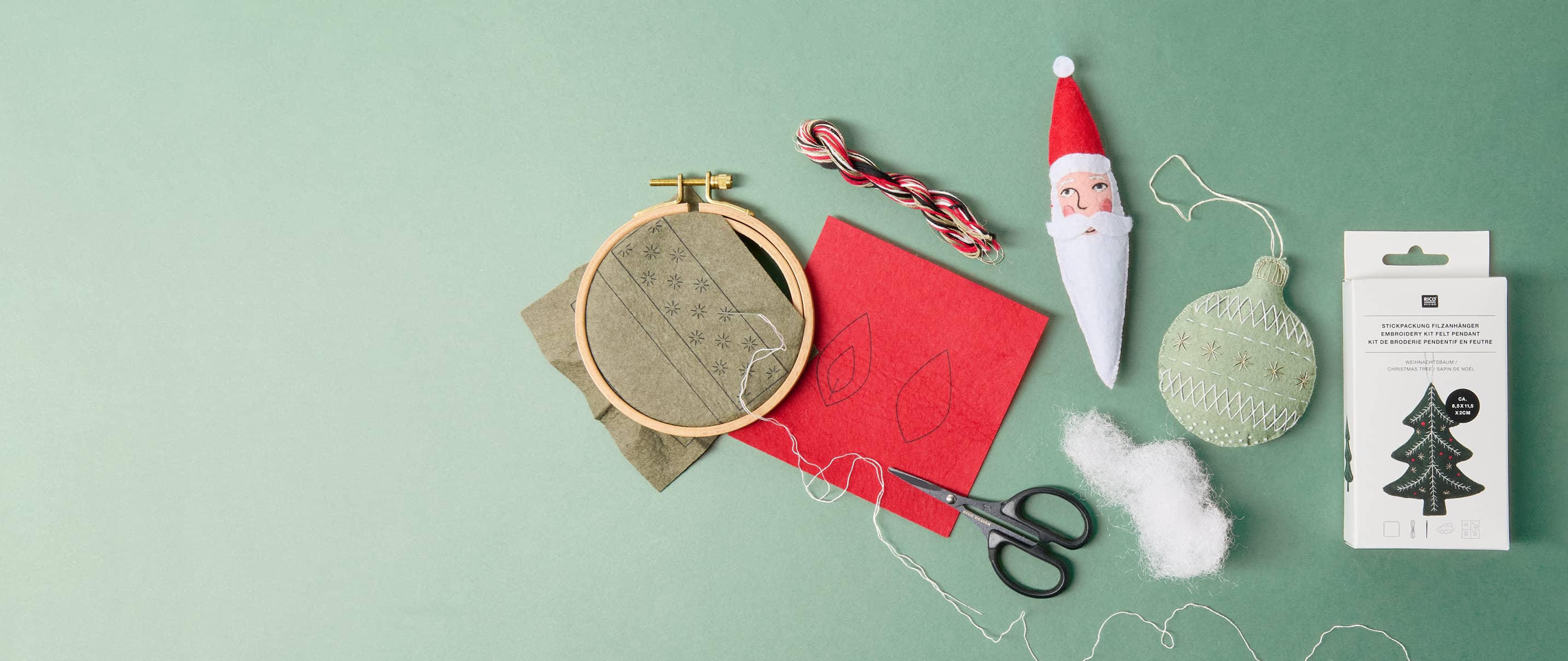 Materialien für gestickte Filzanhänger mit Weihnachtsmotiven, darunter Stickrahmen, Garn, Schere und fertige Anhänger.