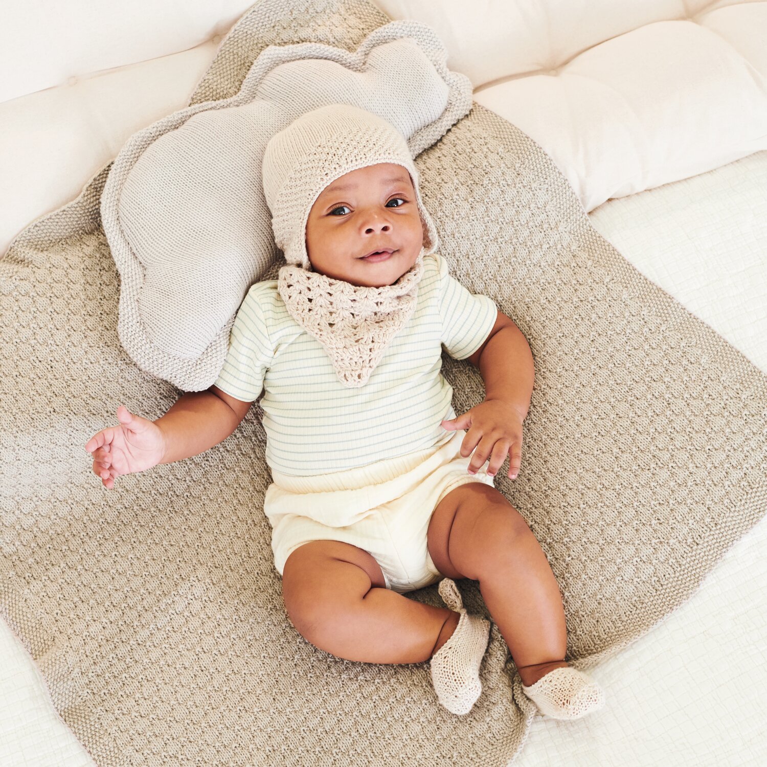 Strickset Mütze Modell 03 aus Baby 043: Baby in cremefarbener Mütze und Schal auf gestrickter Decke.
