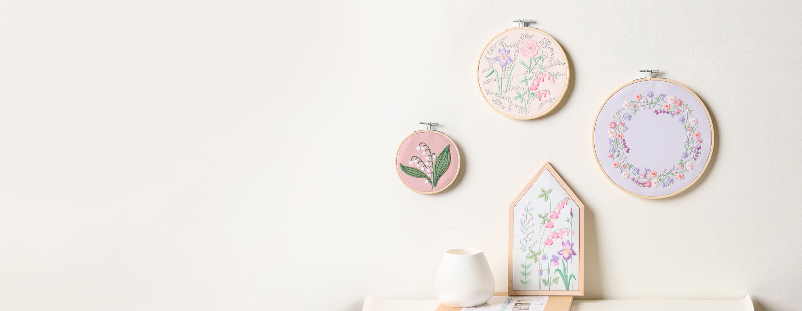 Stickbilder mit floralen Stickdesigns aus der Kollektion The Sky is the Limit hängen an einer Wand.