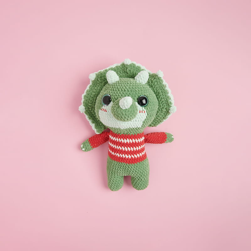 Ein gehäkelter Dinosaurier aus Chenillegarn liegt auf rosa Hintergrund