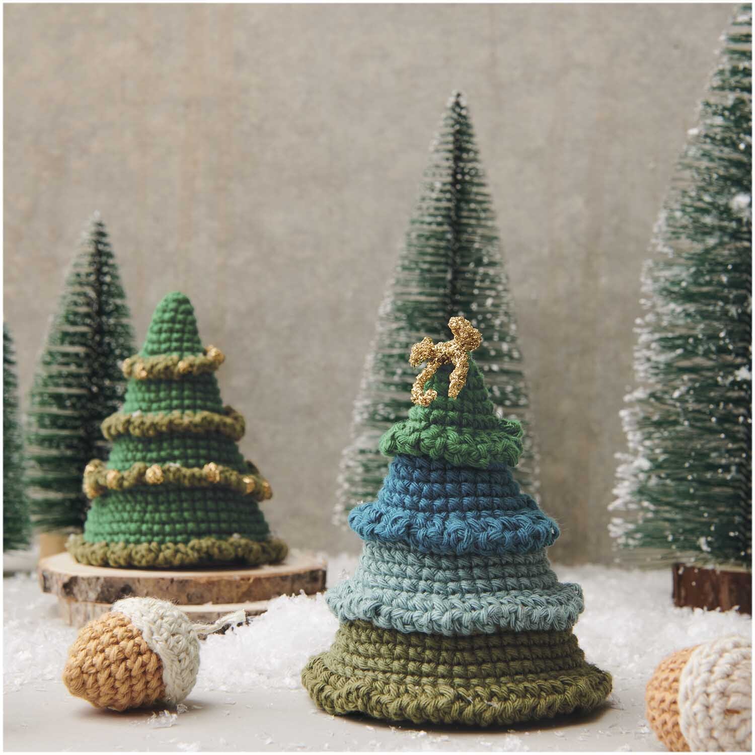 Creative Ricorumi dk: Gehäkelte Tannenbäume in Grün- und Blautönen, dekoriert mit goldenen Details, umgeben von Kunstschnee.