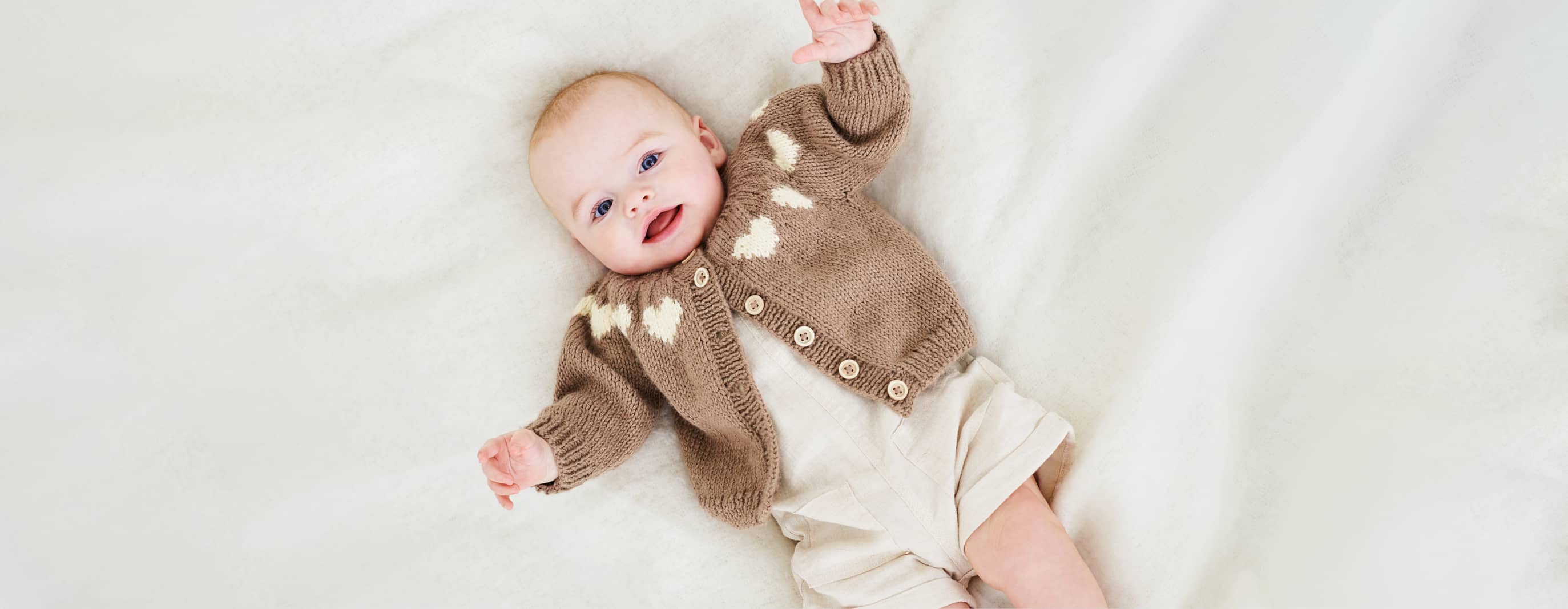Ein Baby liegt mit einer Strickjacke gekleidet auf einer Decke.