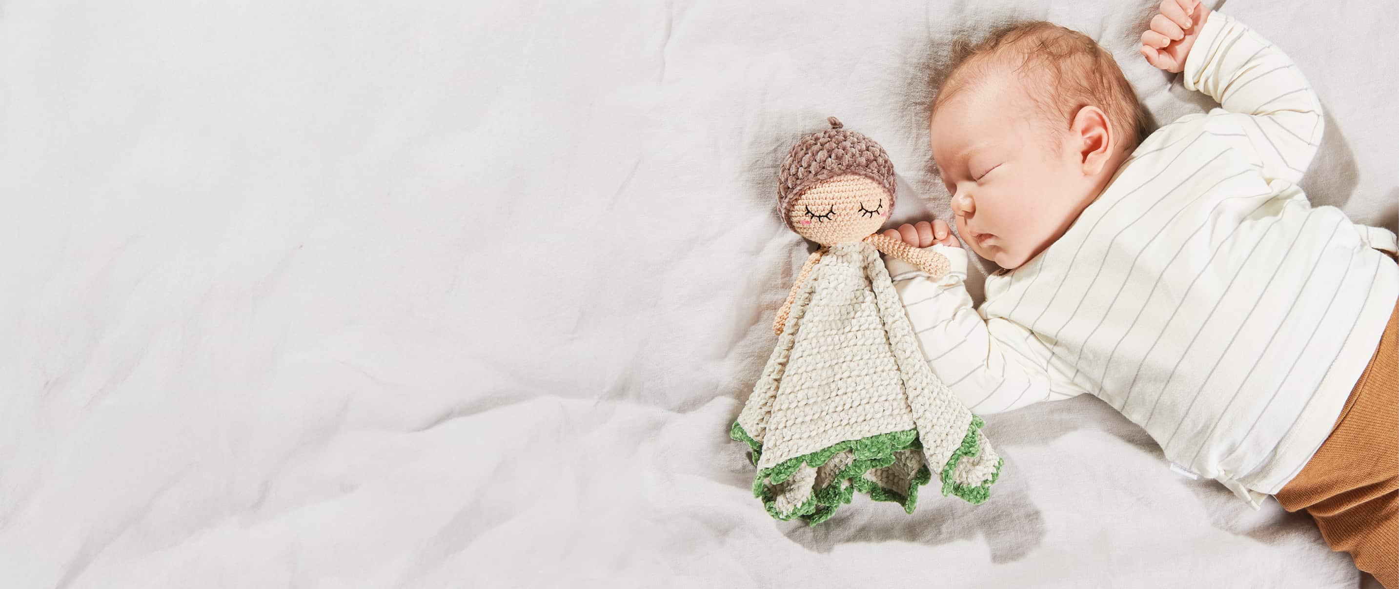 Baby liegt mit gehäkeltem Schmusetuch an der Hand auf einer Decke