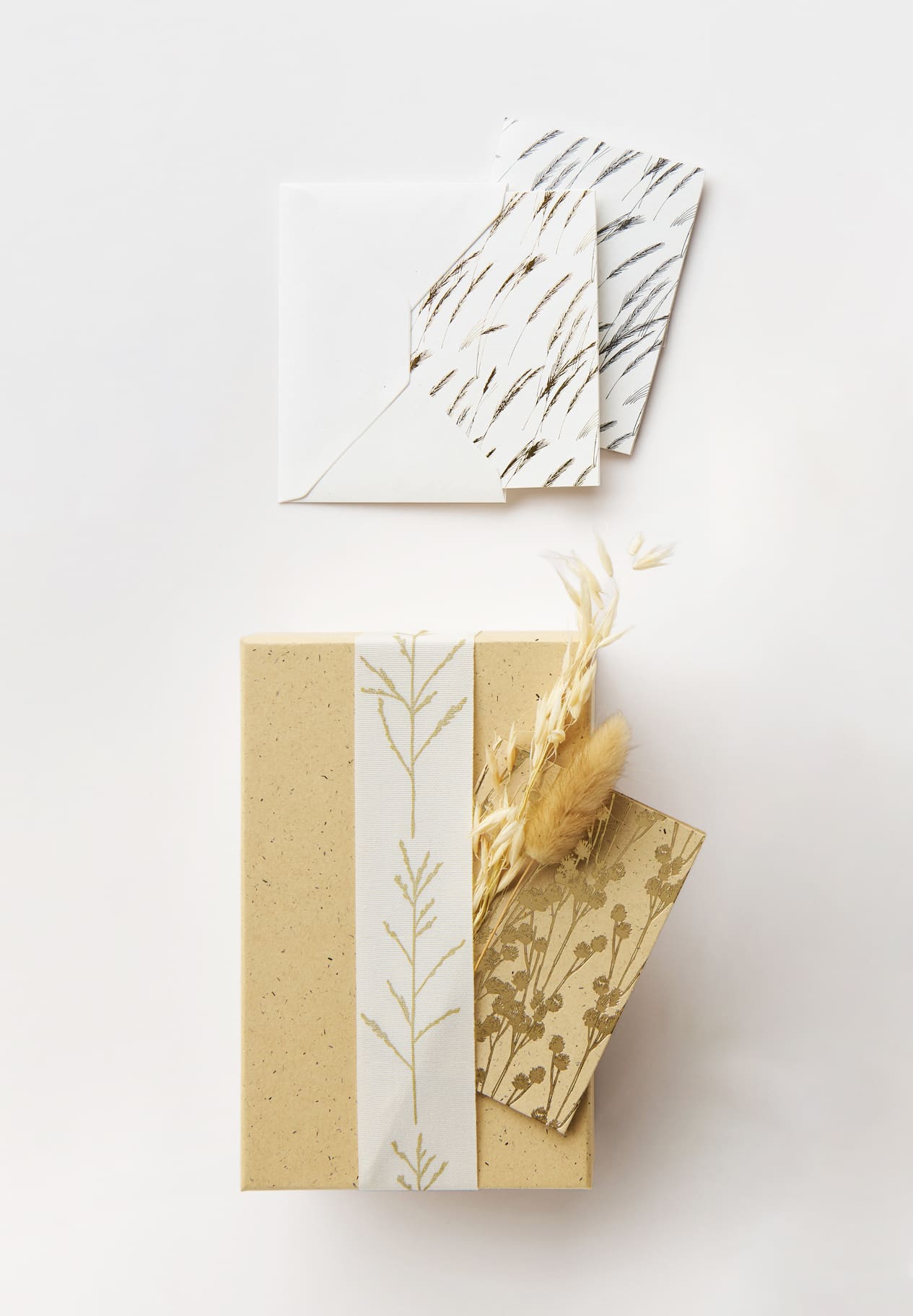 Karten mit goldenen Gräsermotiven liegen auf weißem Hintergrund und an einem Geschenk dekoriert. 