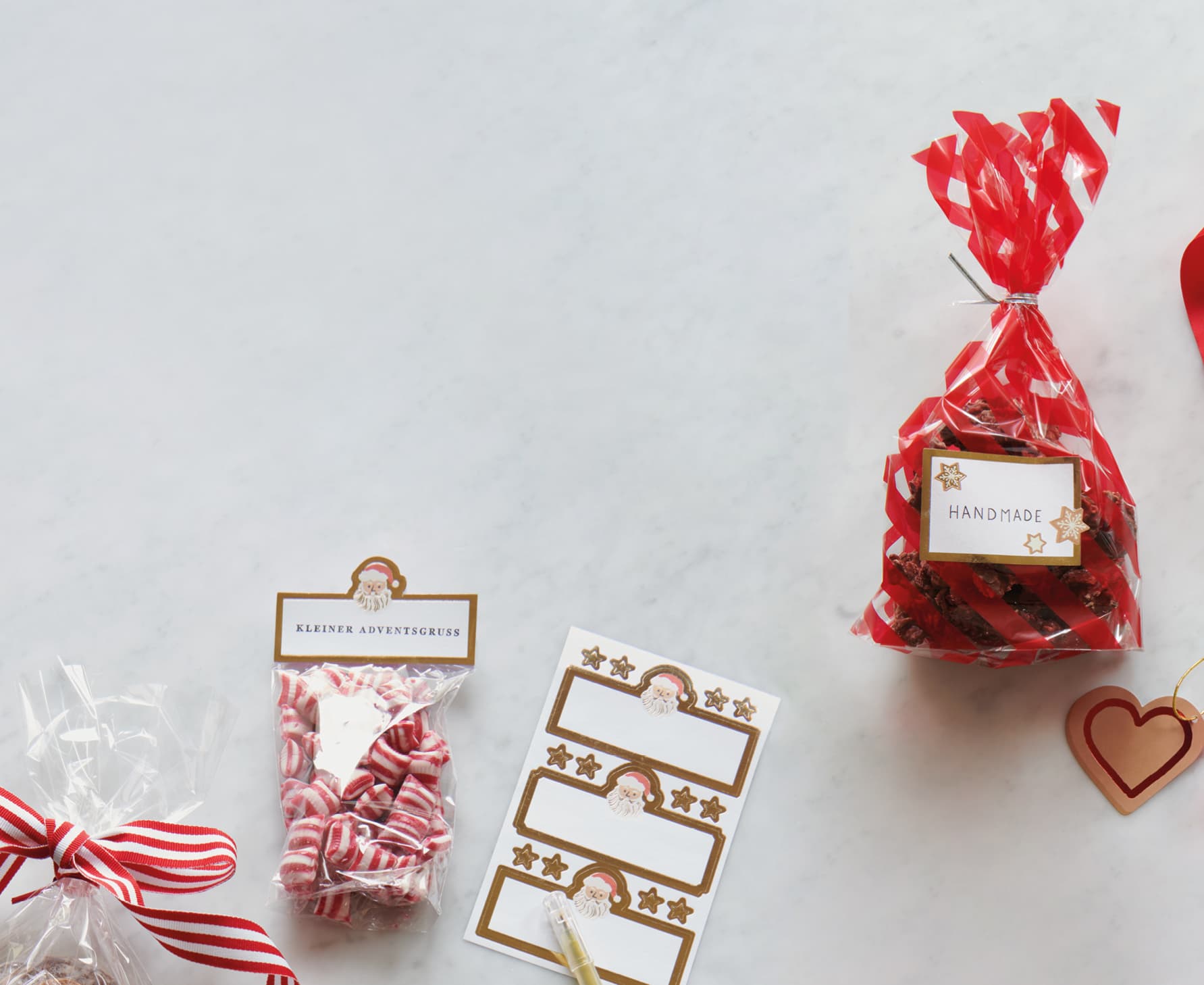 Gefüllte Tüten mit Keksen und Bonbons liegen mit Etiketten-Stickern auf einem Marmor-Untergrund.
