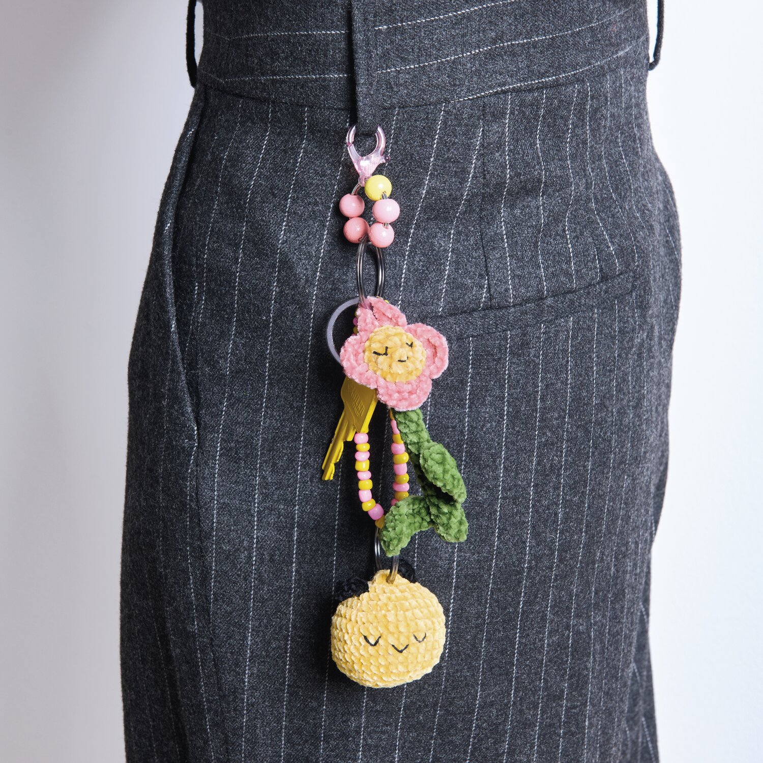 Ricorumi Häkelset Schlüsselanhänger Chingu Earth: Bunter Häkelanhänger an grauem Rock, mit Blumen- und Fruchtmotiven.