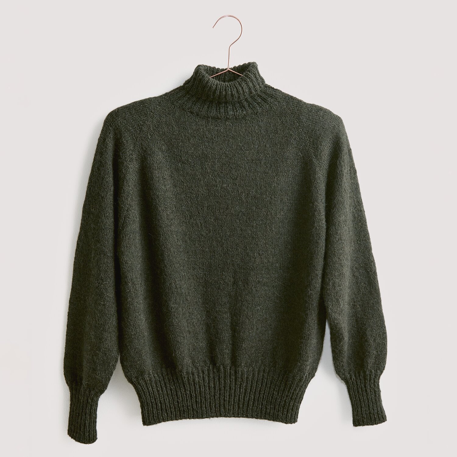 Luxury Knits - Premium Natural Fibres Sprachauswahl deutsch von Rico Design Strickset Pullover Modell 15 aus Luxury Knits. Dunkelgrauer Rollkragenpullover aus Premium Natural Fibres, hängend an einem Kleiderbügel.