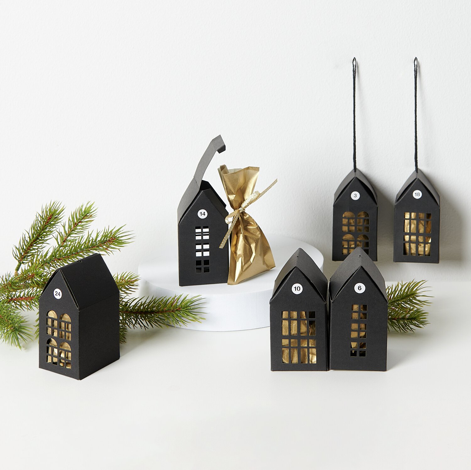 Paper Poetry Papphäuser-Set: Schwarze, vorgestanzte Adventskalender-Häuser von Rico Design, dekorativ aufgestellt mit Tannenzweig.