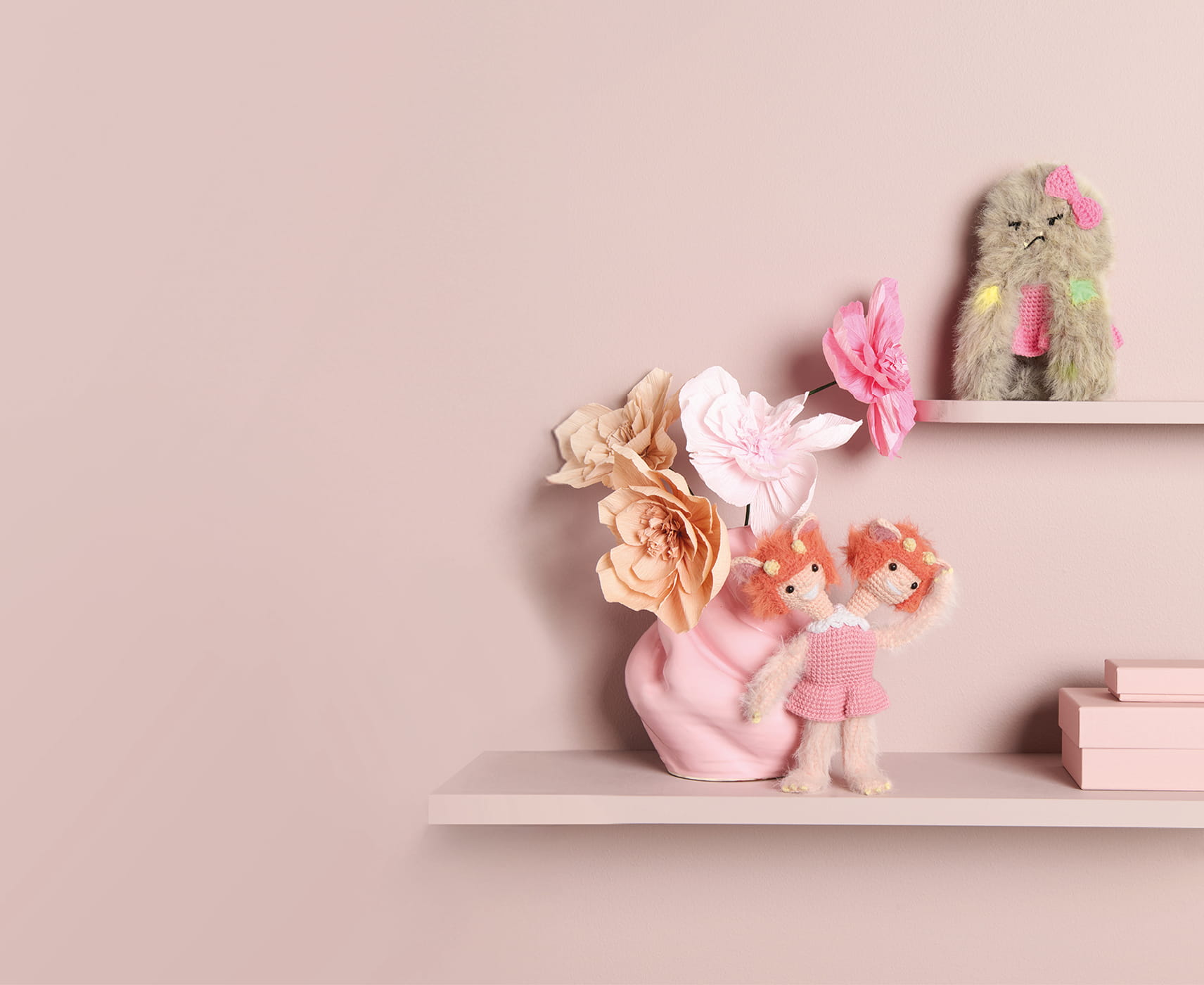 Gehäkelte Monster sind auf Regalbrettern vor einer rosa Wand dekoriert.