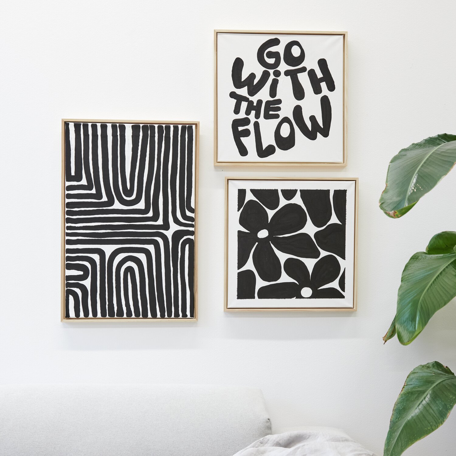 Squeeze Acrylic Marker 60ml: Drei schwarz-weiße Kunstwerke an einer weißen Wand, umgeben von grünen Blättern.