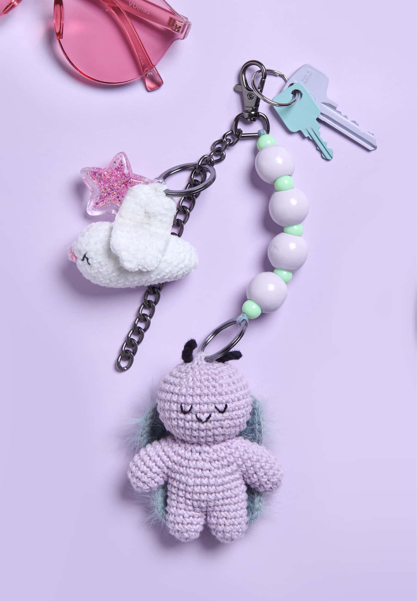 Ein Schlüsselbund mit einem gehäkelten Schmetterling- und einem Vogel-Anhänger liegen auf lila Hintergrund.