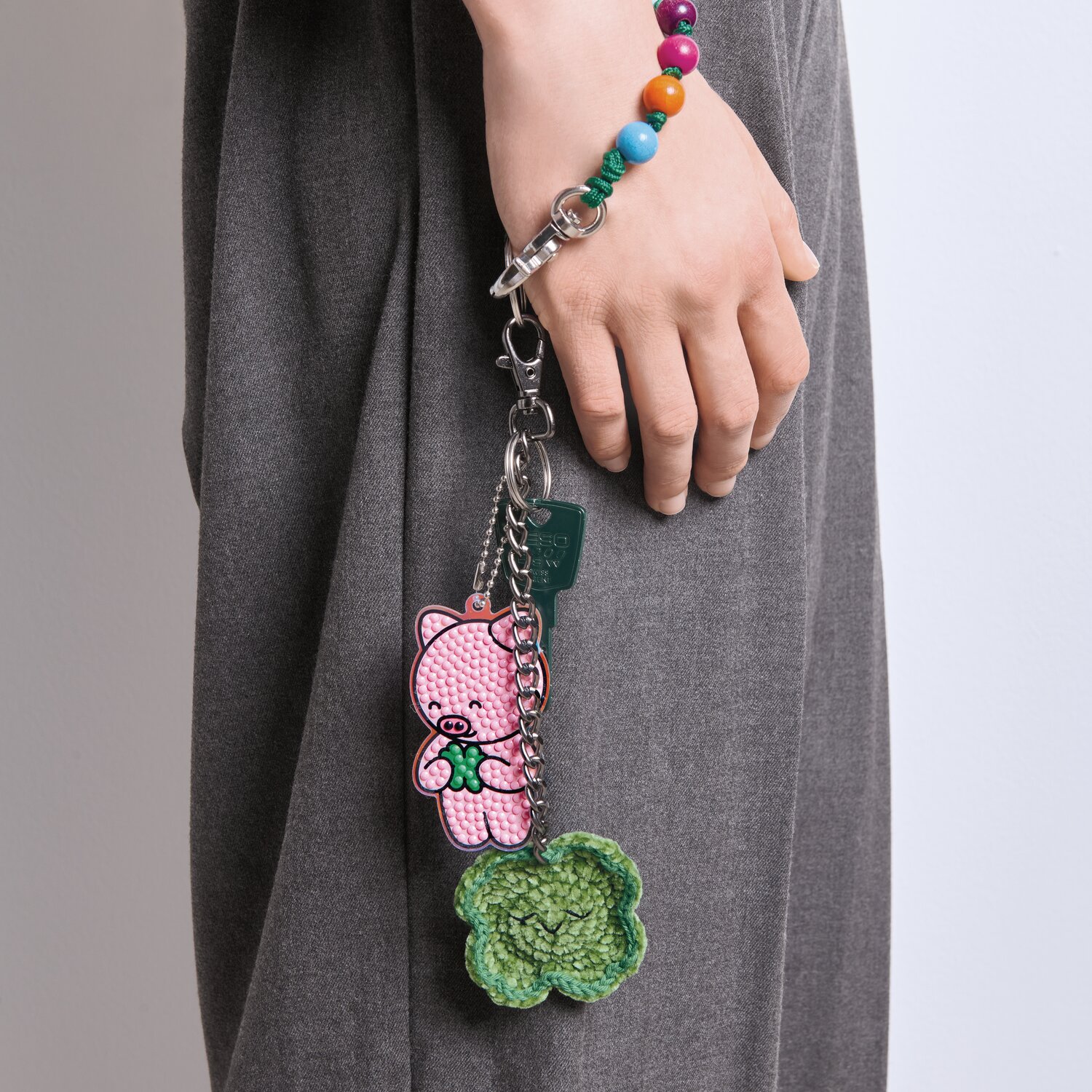 Ricorumi Häkelset Schlüsselanhänger Chingu Earth zeigt einen rosa Bären und grünen Anhänger an grauer Hose.