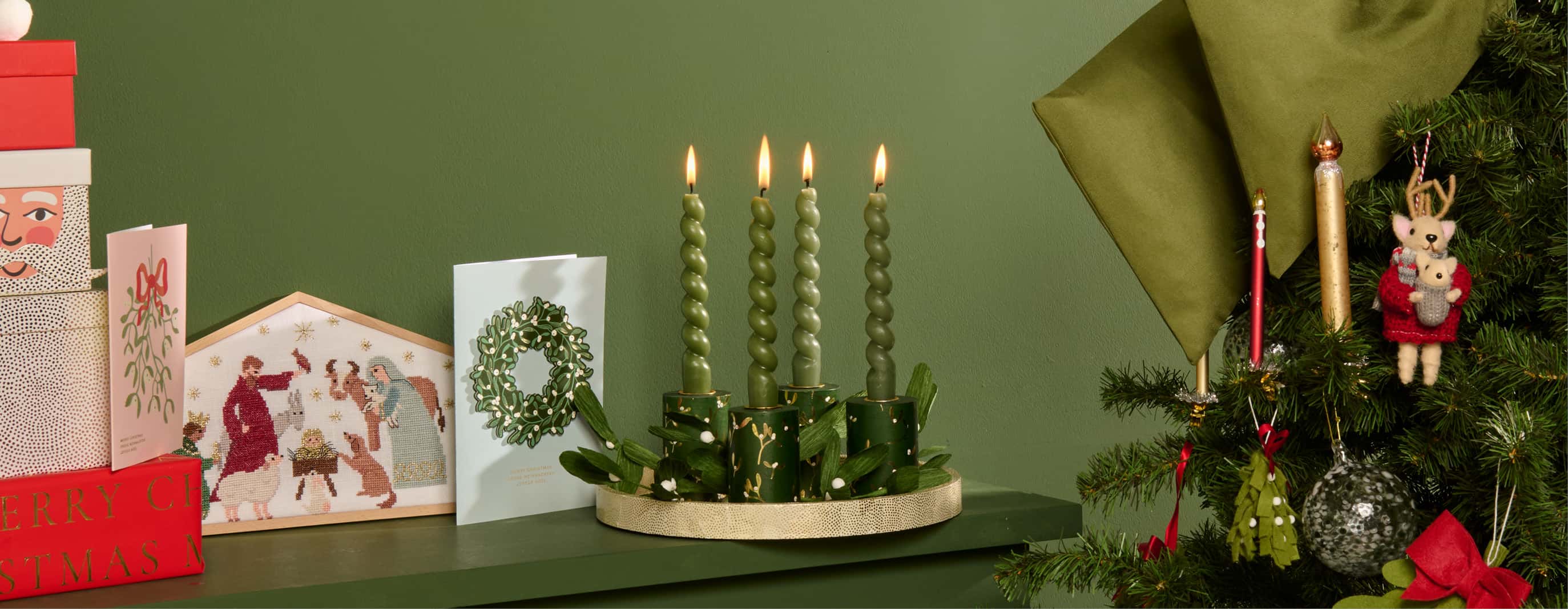 Ein Regal ist weihnachtlich dekoriert mit einem Adventskranz, Weihnachtskarten und Stickbild. Daneben ein geschmückter Weihnachtsbaum.