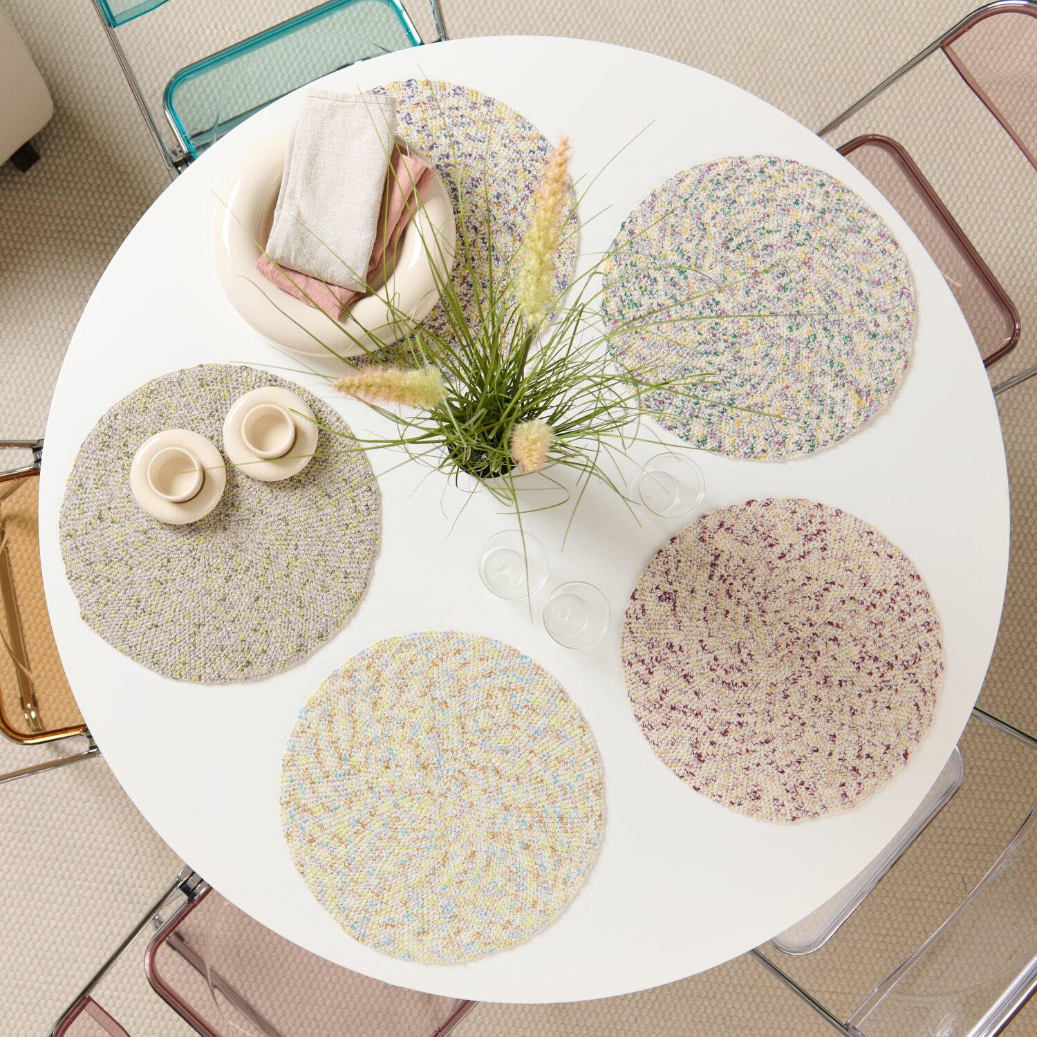 Häkelset Platzset Modell 17: Runde, bunte Platzsets auf weißem Tisch, dekoriert mit Kerzen und Pflanzen.