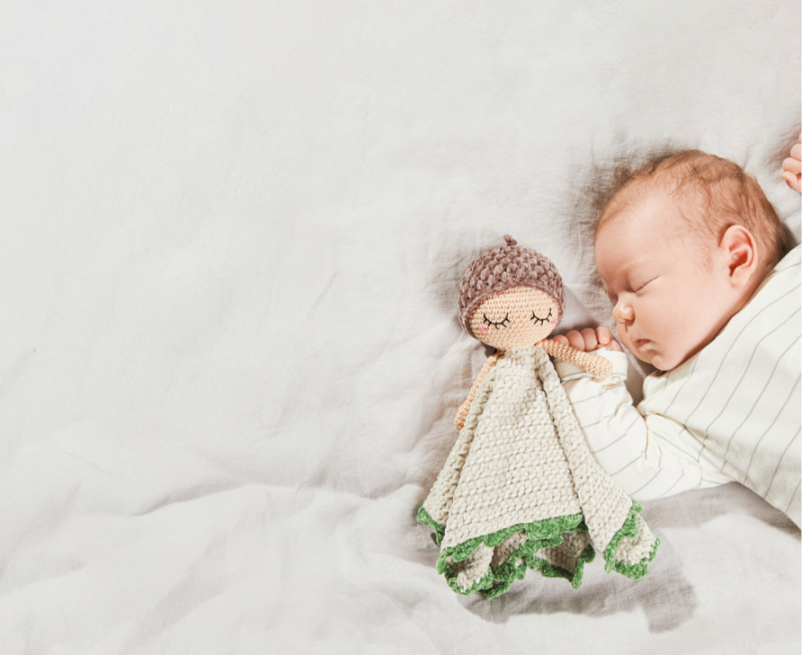 Baby liegt mit gehäkeltem Schmusetuch an der Hand auf einer Decke