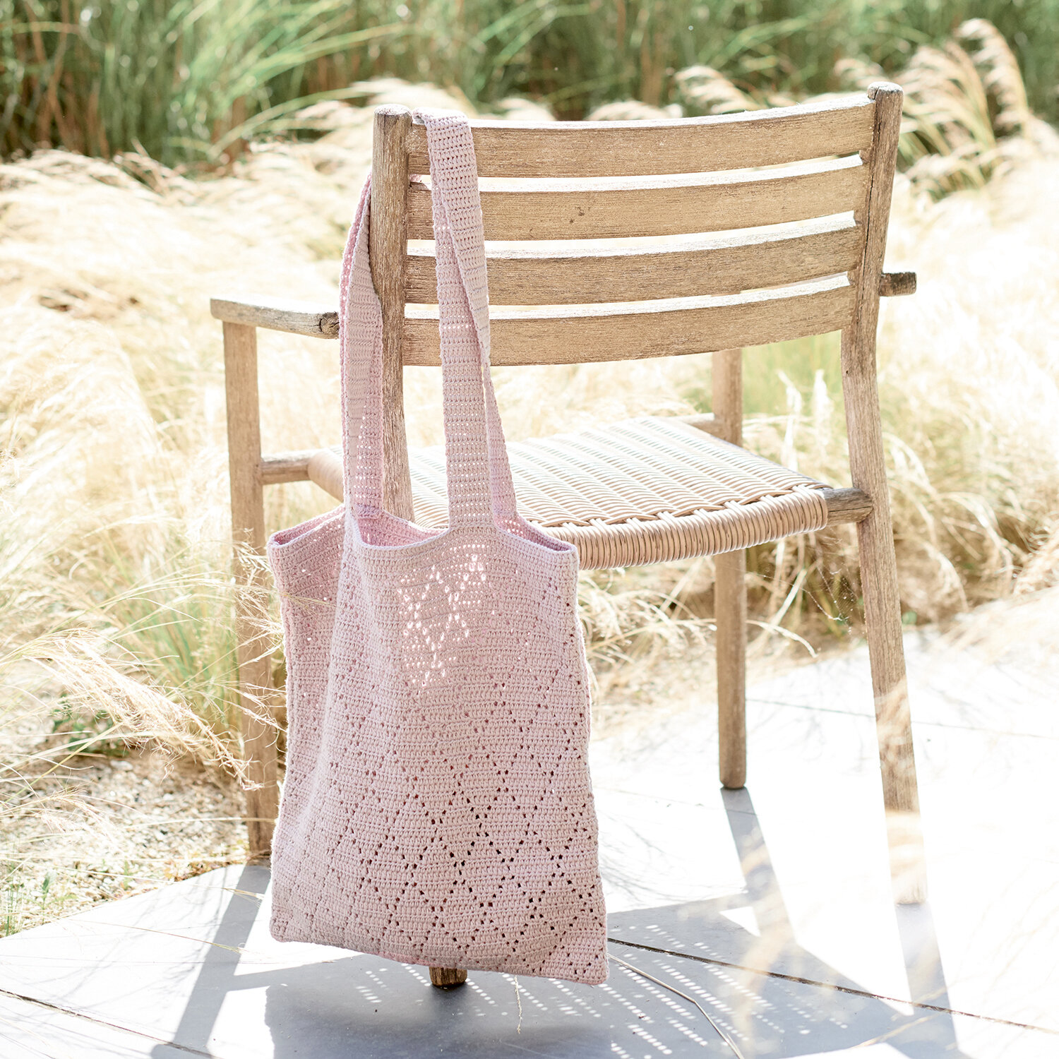 Häkelanleitung Lochmuster-Tasche aus Essentials Organic Cotton aran, leichte Schultertasche mit Lochmuster im Outdoor-Setting an Holzstuhl vor hohen Gräsern