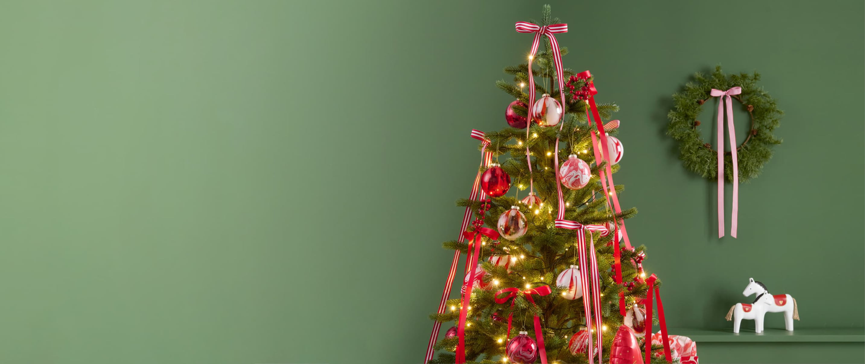 Ein geschmückter Weihnachtsbaum mit Weihnachtskugeln und Schleifen steht vor einem grünen Hintergrund. 