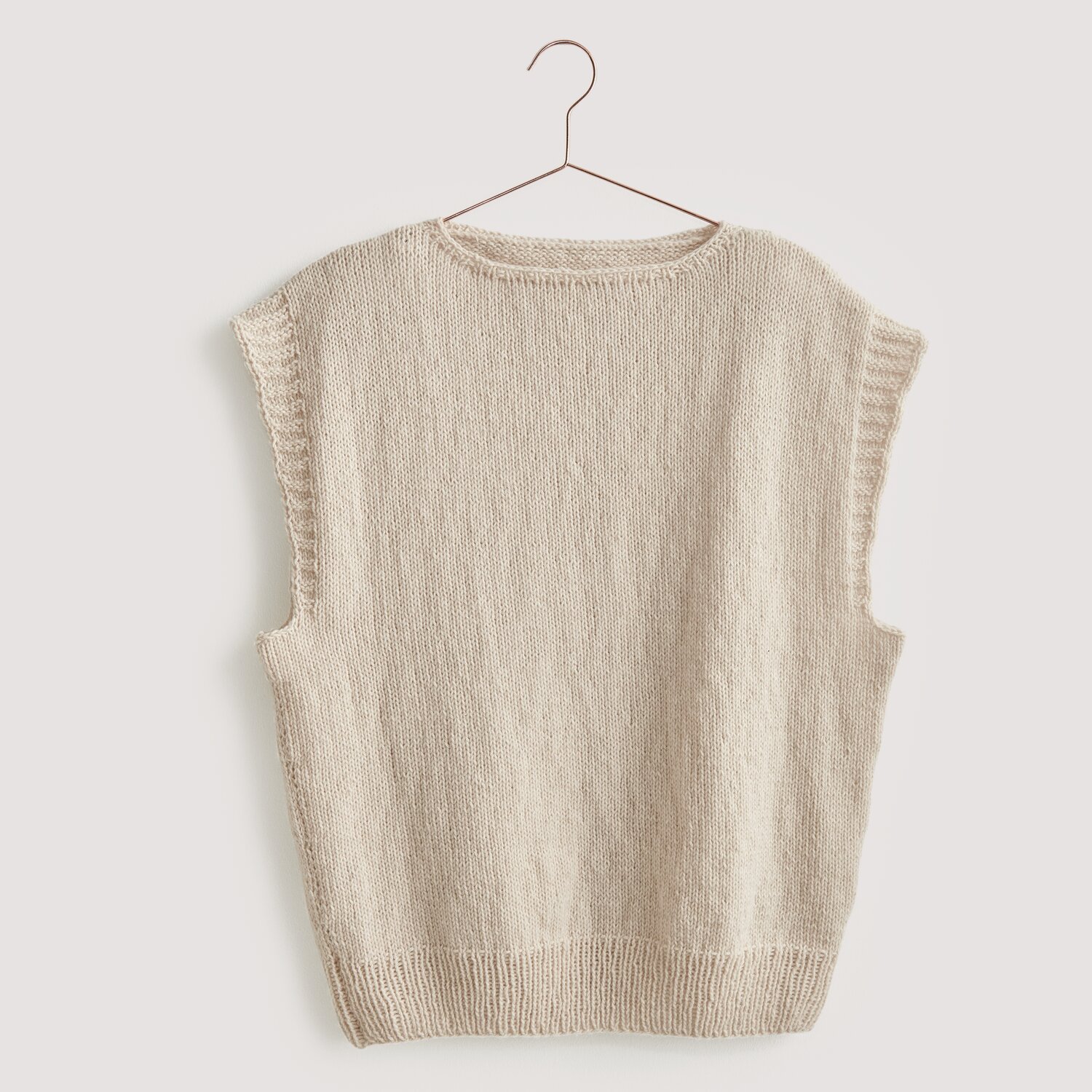Luxury Knits - Premium Natural Fibres Sprachauswahl deutsch von Rico Design Strickset Pullunder Modell 03 aus Luxury Knits: Beiger Pullunder aus Premium Natural Fibres, hängend an einem Kleiderbügel.