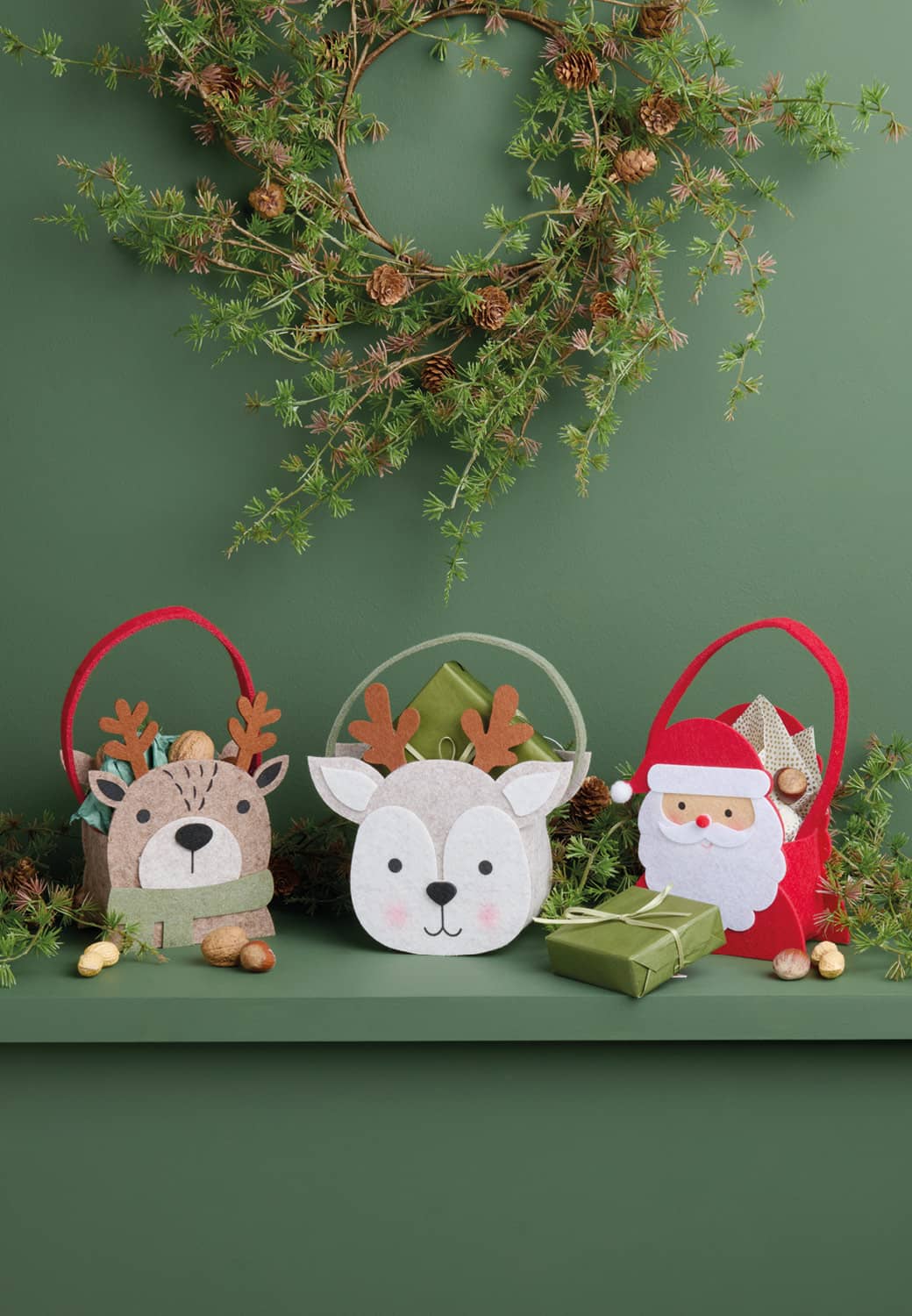 Drei Filzkörbe in Form von einem Weihnachtsmann und zwei Hirschen stehen auf einem weihnachtlich dekoriertem Regal.