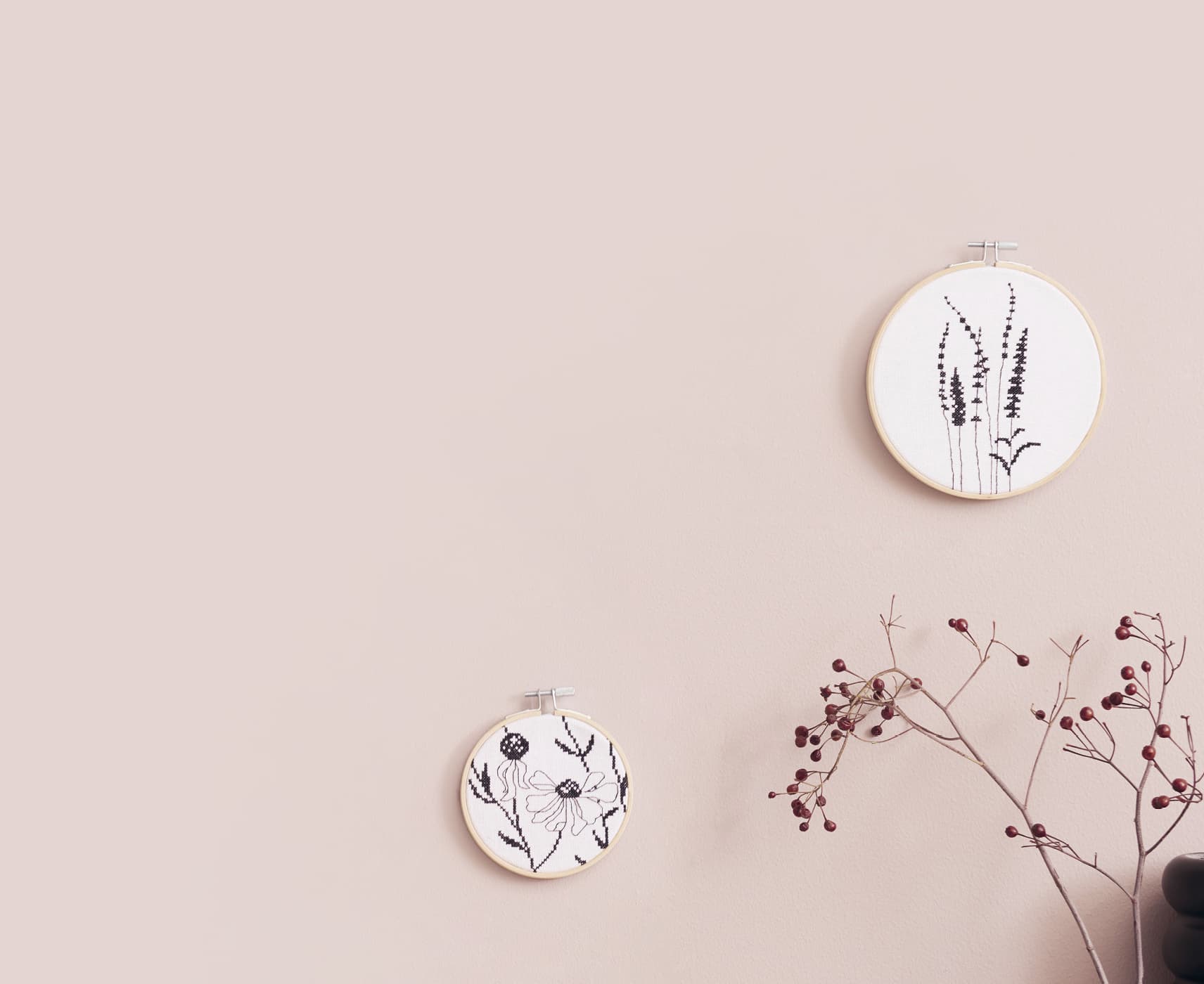 Stickbilder mit Gräser- und Blumenmotiven hängen an einer beigen Wand. 
