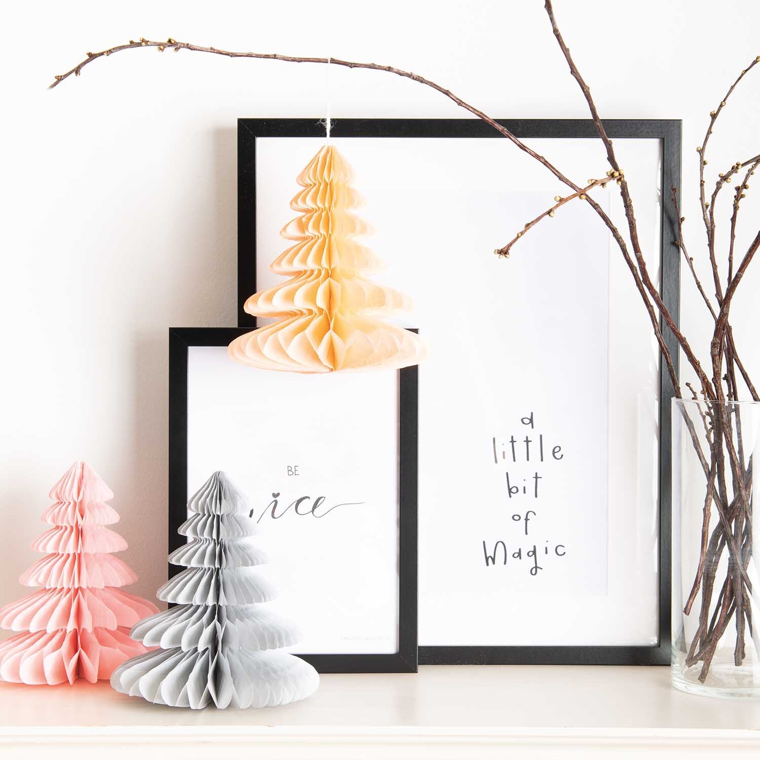 Wabenpapier Tannenbäume 20cm 3 Stück Farbe Pastell von Rico Design Wabenpapier Tannenbäume 20cm 3 Stück in Pastellfarben vor gerahmten Bildern und Zweigen.
