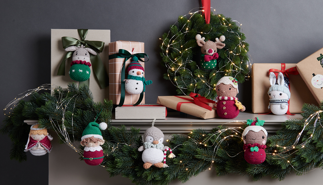 Häkelanleitung Ricorumi Rentier Weihnachten: Festliche Dekoration mit gehäkelten Figuren und Lichterkranz auf einem Kaminsims.