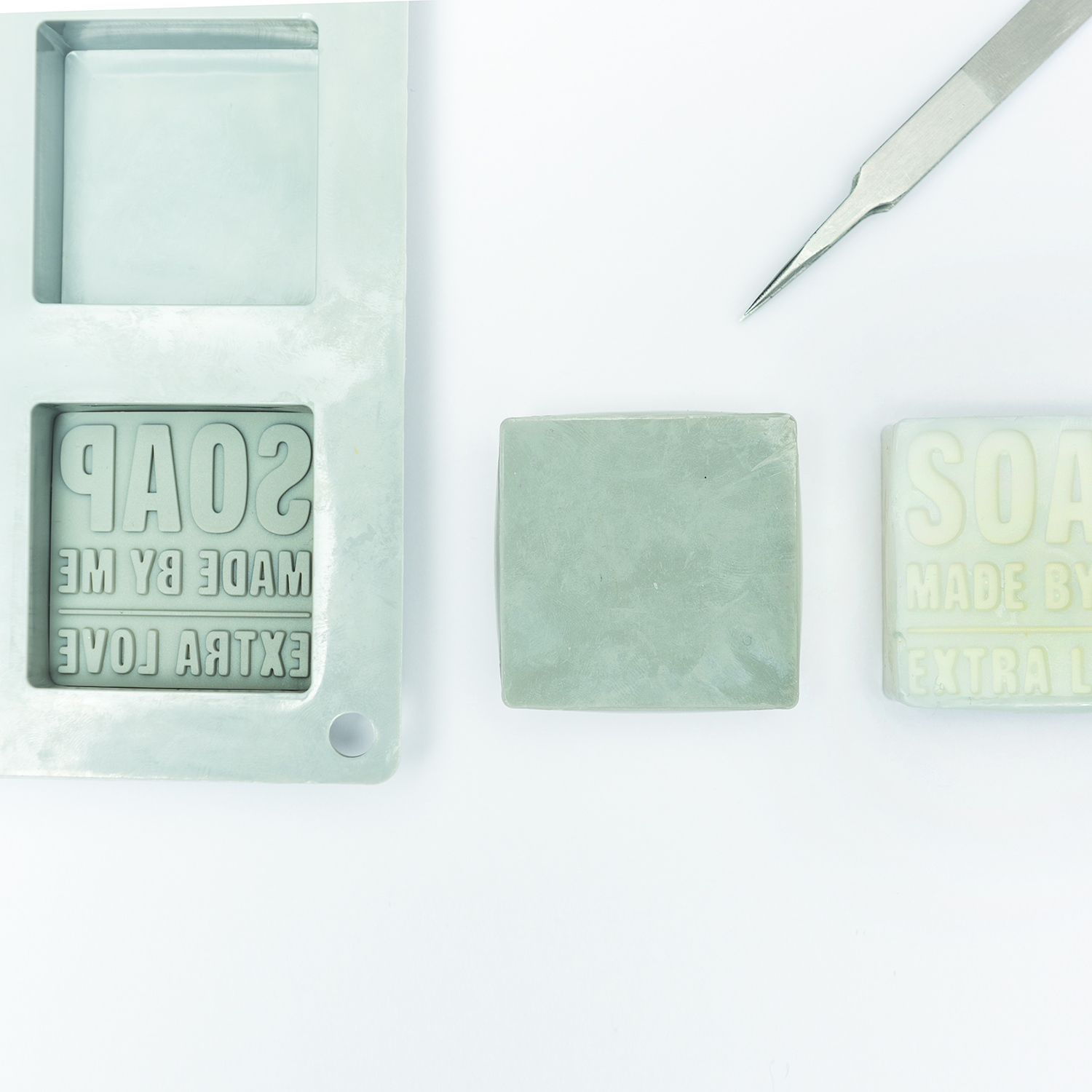 Eine Prägeform mit Schriftzug "Soap Made by Me" liegt in einer Seifengießform. Daneben ein Stück Seife mit genannter Prägung
