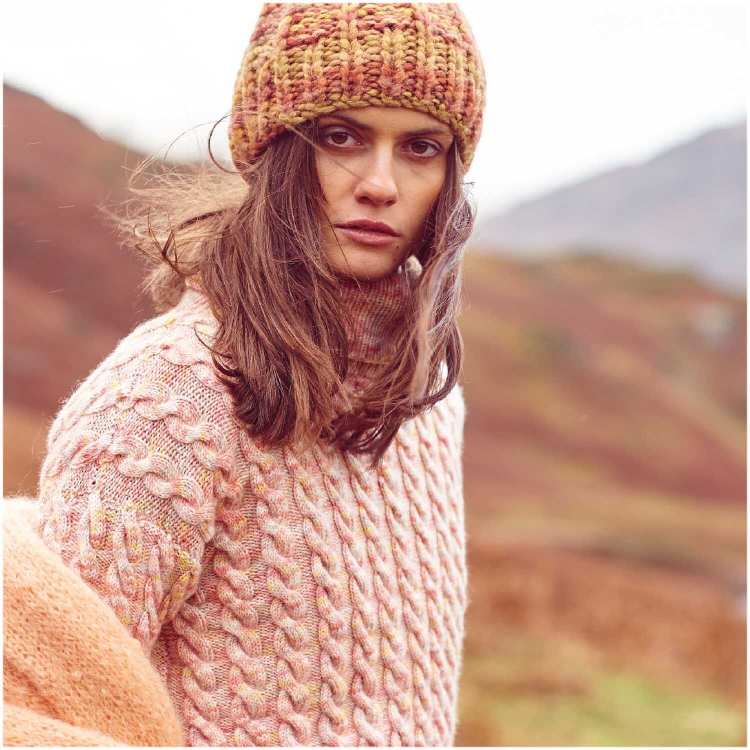 Luxury Hand-Dyed Happiness dk: Frau in gestricktem Pullover und Mütze in herbstlicher Landschaft.