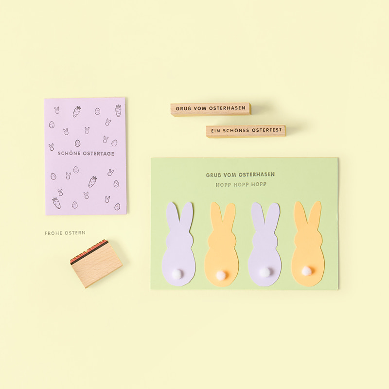 Zwei gebastelte Osterkarten liegen umgeben von Stempeln auf gelbem Hintergrund.