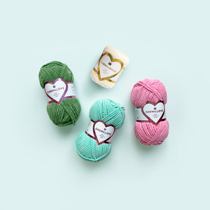 Chenille Knäuel in verschiedenen Farben liegen auf hellblauem Hintergrund