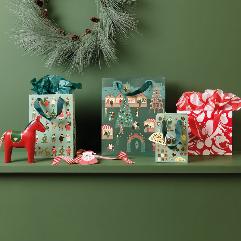 Geschenktüten in verschiedenen Formaten mit weihnachtlichen Designs dekoriert auf einem Kaminsims