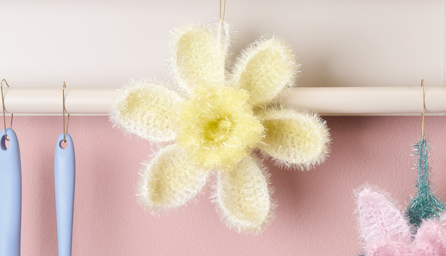 Häkelanleitung Narzisse aus Creative Bubble Dégradé: Gelbe Blume mit flauschiger Textur an rosa Wand.