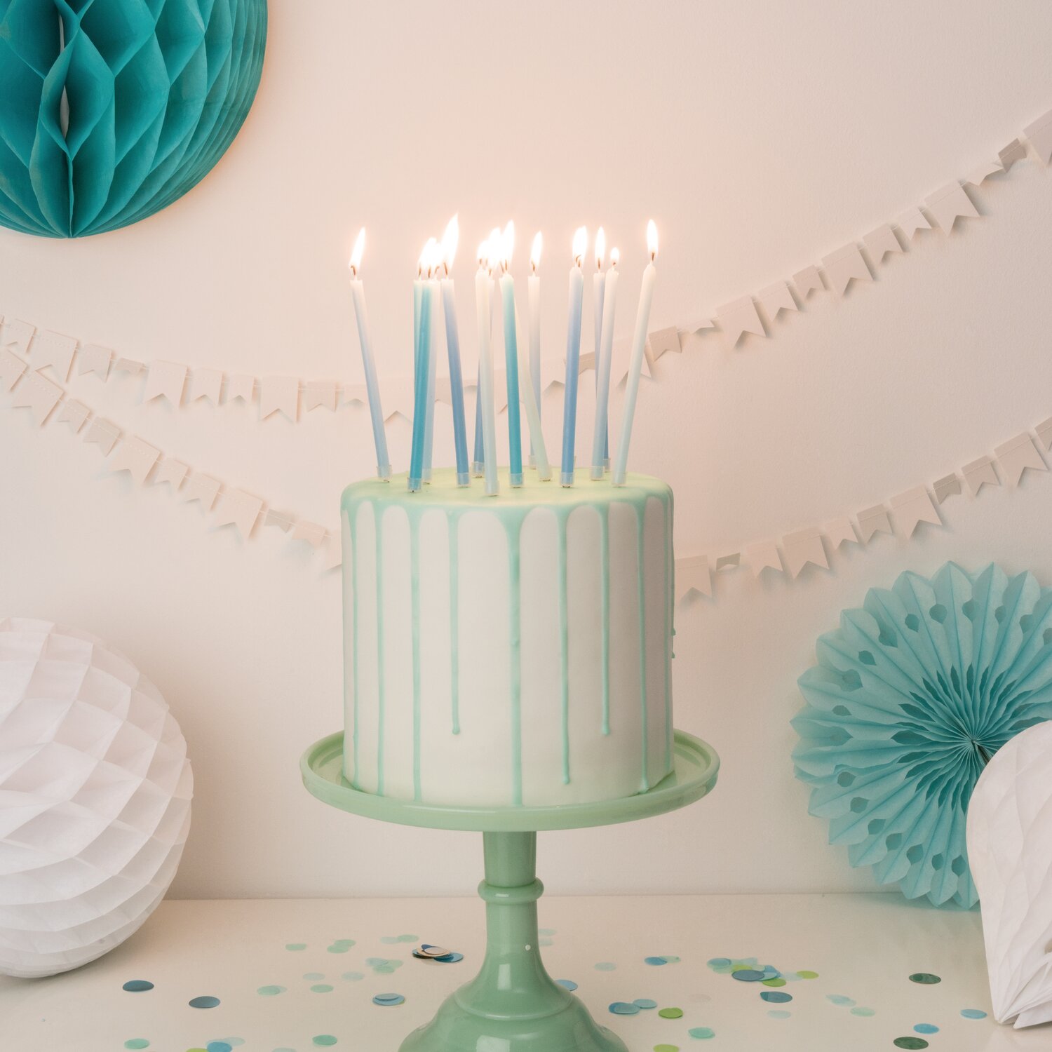 Kerzen lang 12cm, 16 Stück von Rico Design auf Geburtstagstorte, pastellige Zierkerzen auf Ständer, Partydeko mit Konfetti und Wabenbällen im Hintergrund