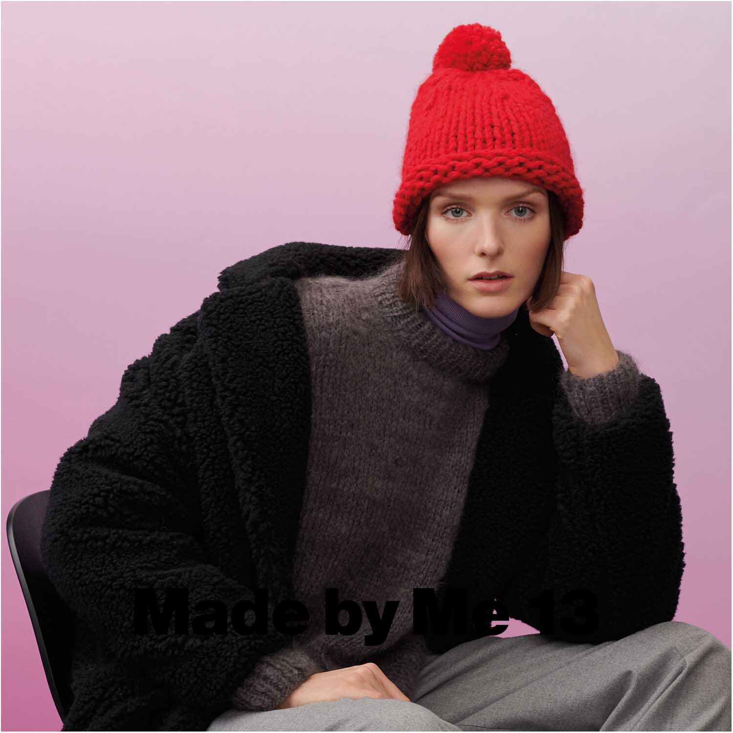 Fashion Alpaca Cozy Up! Frau in rotem Strickhut und schwarzem Mantel von Rico Design vor rosa Hintergrund.