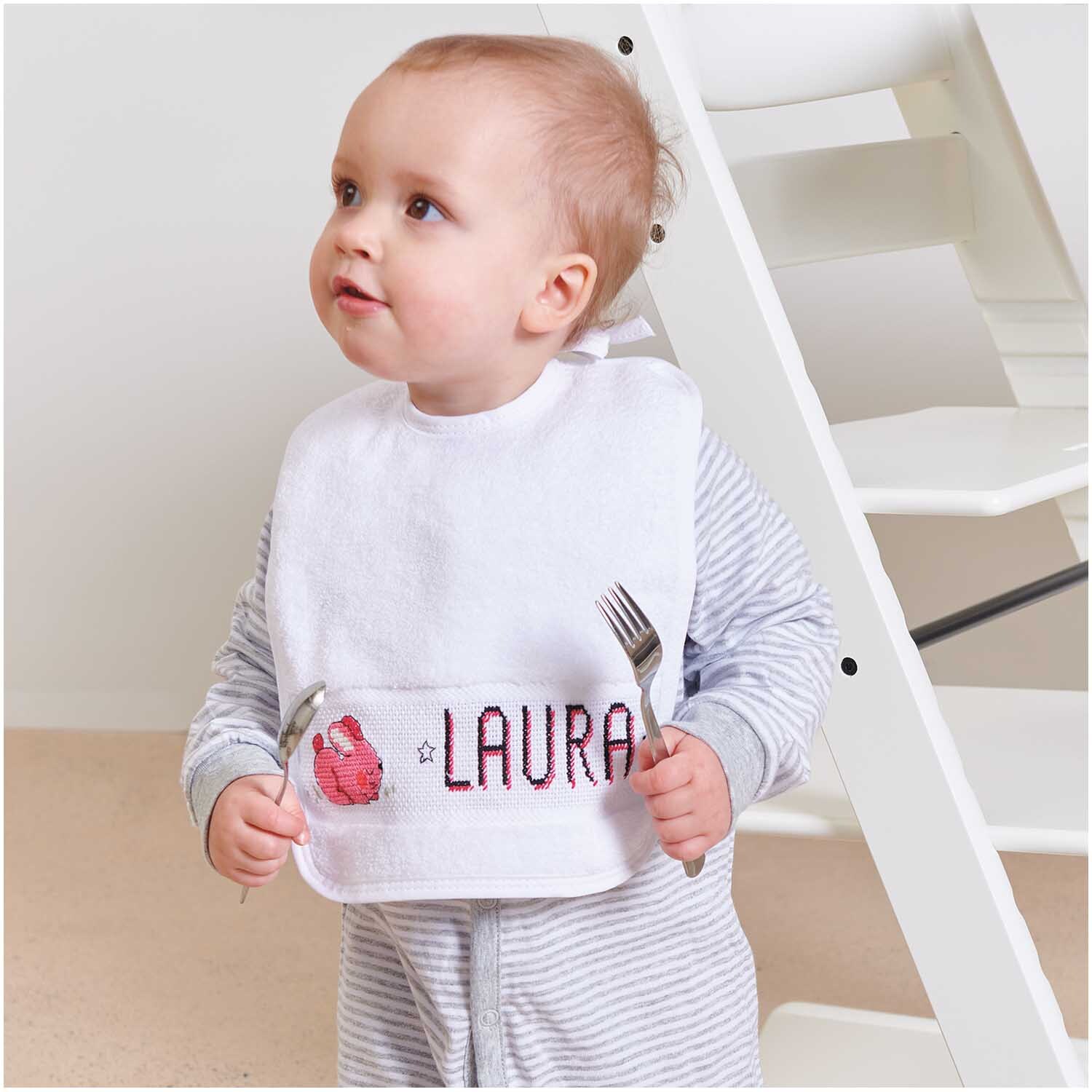 Lätzchen 30x34cm Farbe Weiß von Rico Design Lätzchen weiß 23x28cm: Ein Baby trägt ein weißes Lätzchen von Rico Design, während es auf einem Hochstuhl sitzt.