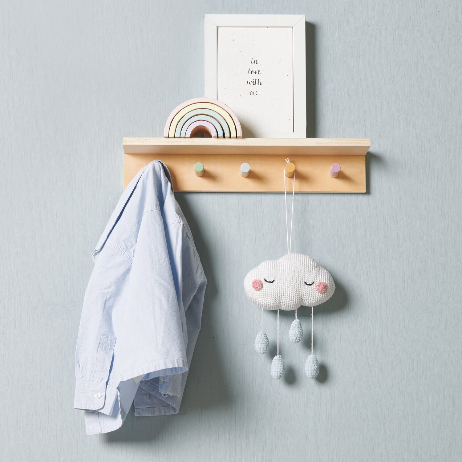 Ricorumi Glow In The Dark: Holzregal mit bunter Wolken-Deko und hellblauem Hemd an Haken.