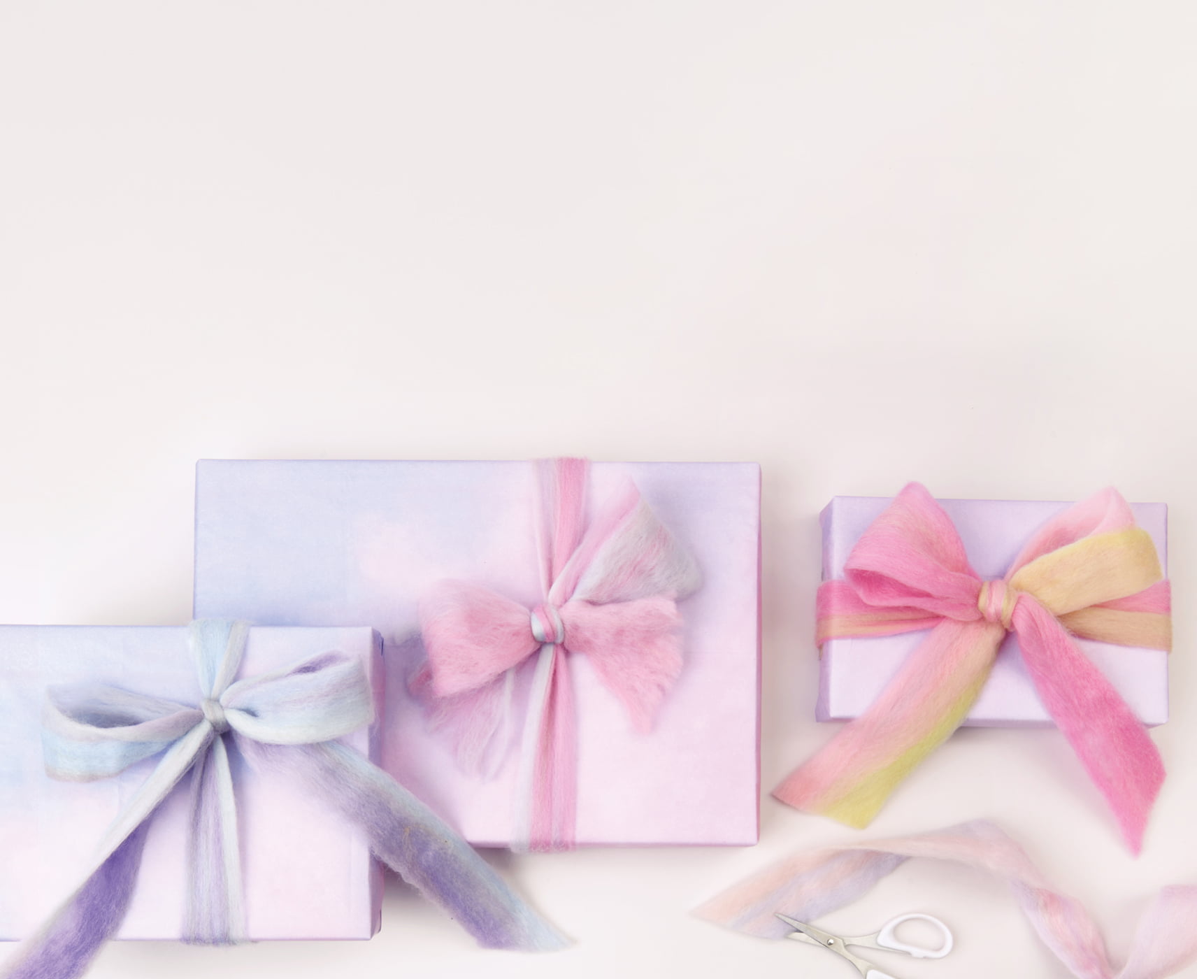 Verpackte Geschenke in Pastelltönen sind mit Filzband geschmückt. 