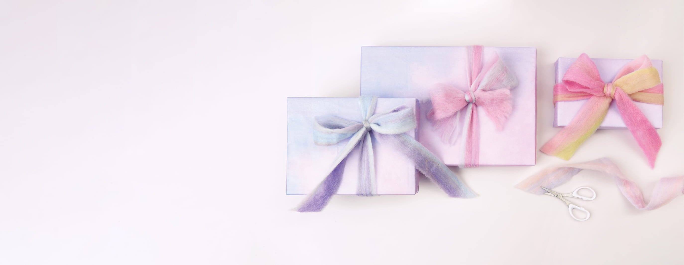 Verpackte Geschenke in Pastelltönen sind mit Filzband geschmückt. 