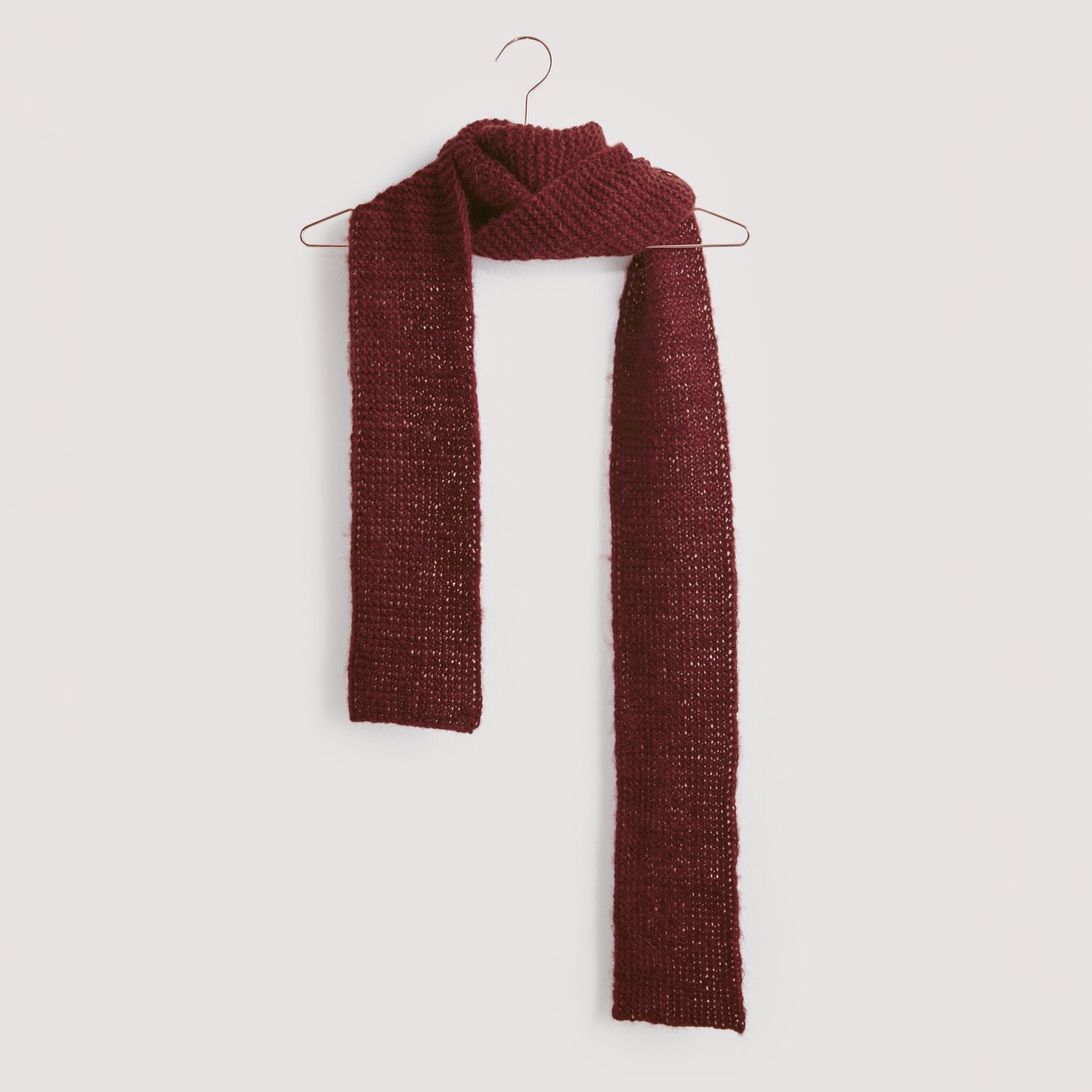 Luxury Knits - Premium Natural Fibres Sprachauswahl deutsch von Rico Design Strickset Schal Modell 17 aus Luxury Knits, dunkelroter Schal aus Premium Natural Fibres, hängt an einem Kleiderbügel vor grauem Hintergrund.
