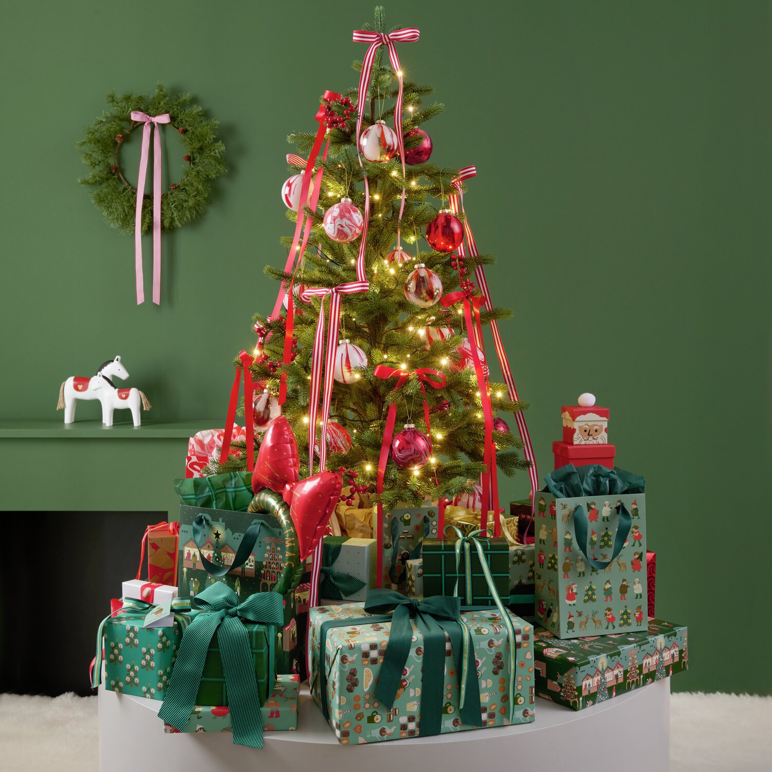 Weihnachtlich dekorierter Raum mit einem geschmückten Baum und Geschenken. Das Geschenkpapier von Rico Design, "Paper Poetry Weihnachtsmarkt Mix", zeigt festliche Muster in verschiedenen Farben.