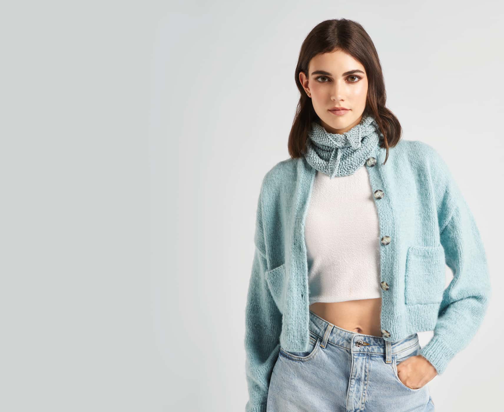 Eine Frau trägt gestrickte Jacke und Halstuch in hellblau.