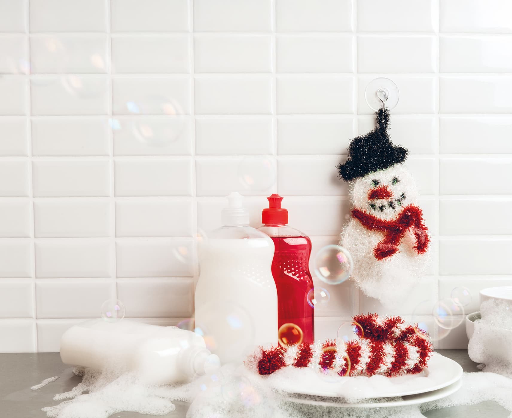 Gehäkelte Spülschwämme in Form von Schneemann und Zuckerstange sind an einem Spülbecken dekoriert